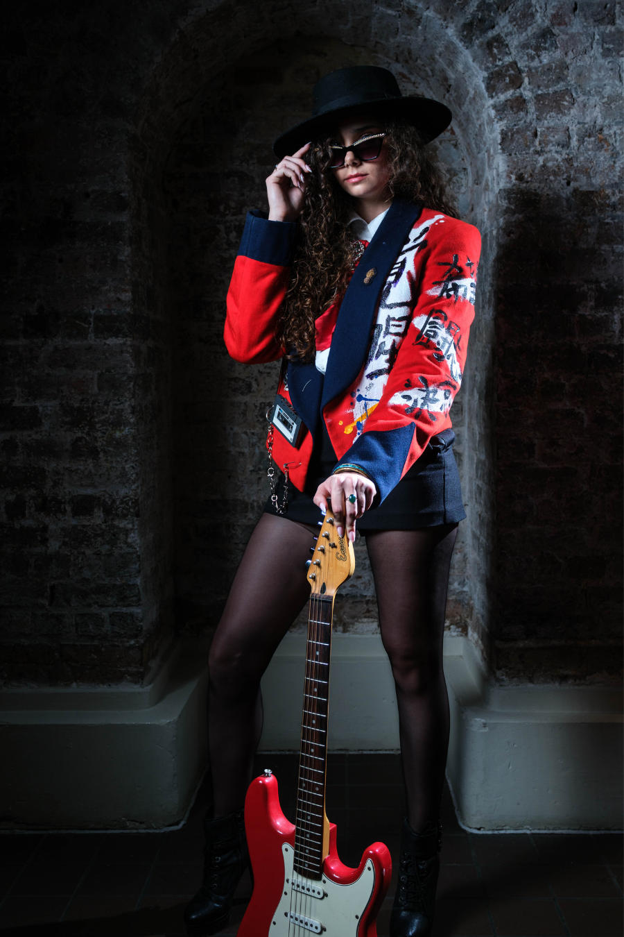 Lady Diana Velvet Art Jacket in red velvet with navy lapels, abstract black and white artwork, worn by model holding red electric guitar.